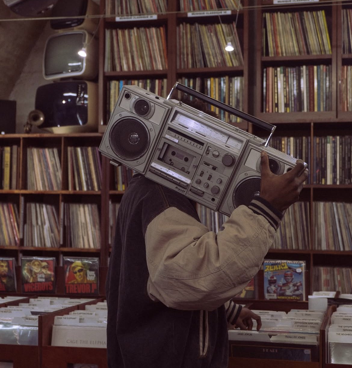 Un client, blouson teddy sur le dos, porte un boombox à l'épaule devant les bacs à disques.