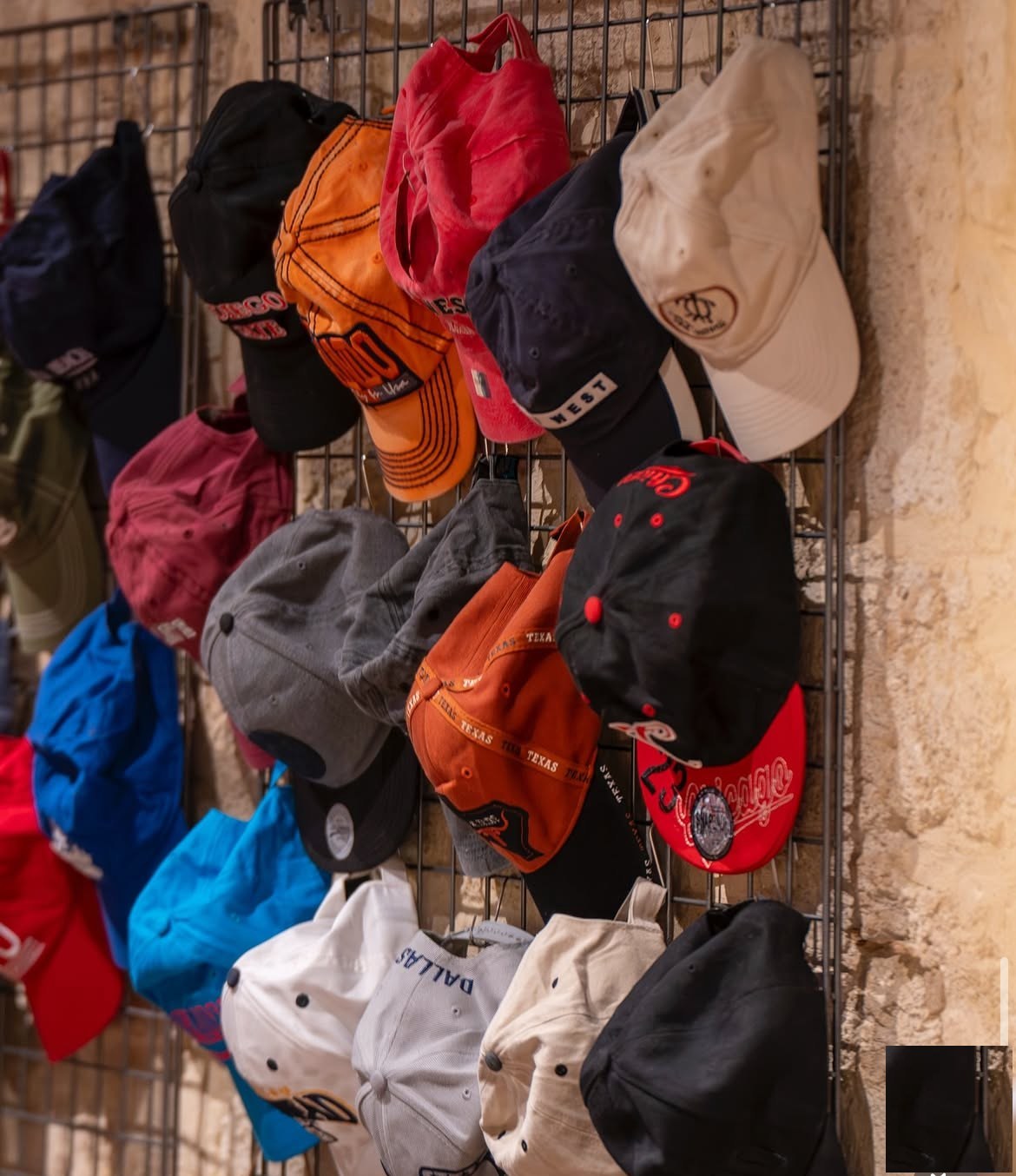 Un mur de casquettes vintage accrochées à une grille, sur la pierre de la boutique.