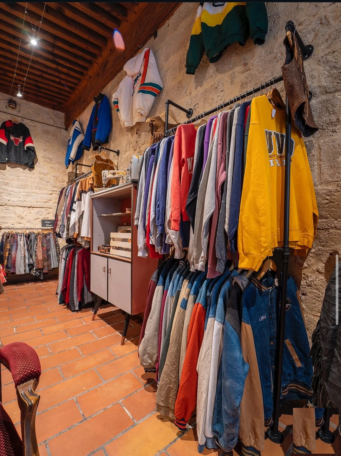 Racks de vêtements vintage sous les voûtes en pierre : sweats universitaires, blousons baseball, vestes en denim.